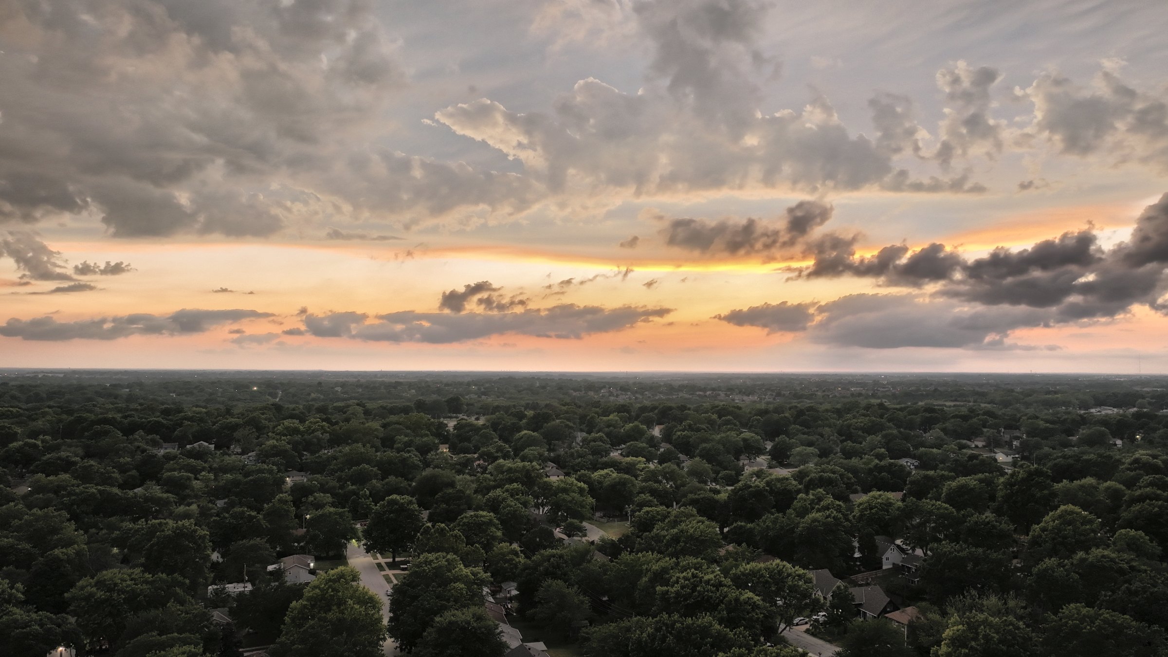 Dusk aerial over a mature tree canopy in a Kansas City metro suburb