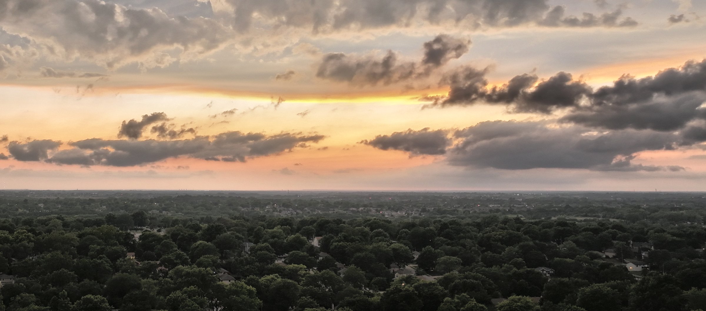 Evening aerial of rooftops among mature trees in the Kansas City metro