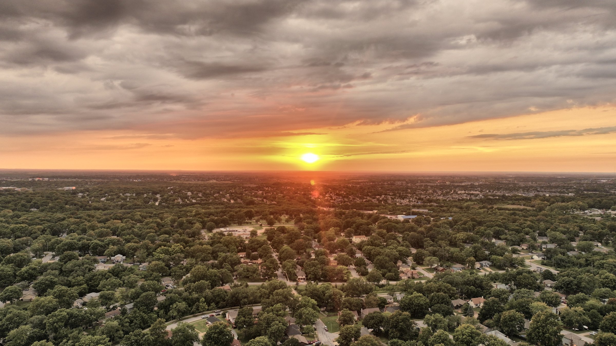 Sunset aerial over tree-lined suburban streets in the Kansas City metro